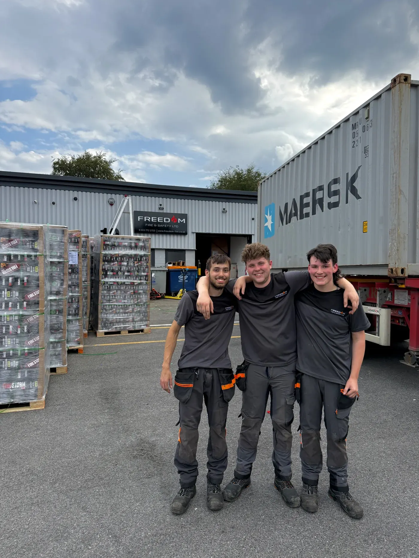 Three of the warehouse team in front of a container being unloaded at Unit 19, pallets of Firestorm stock beside them